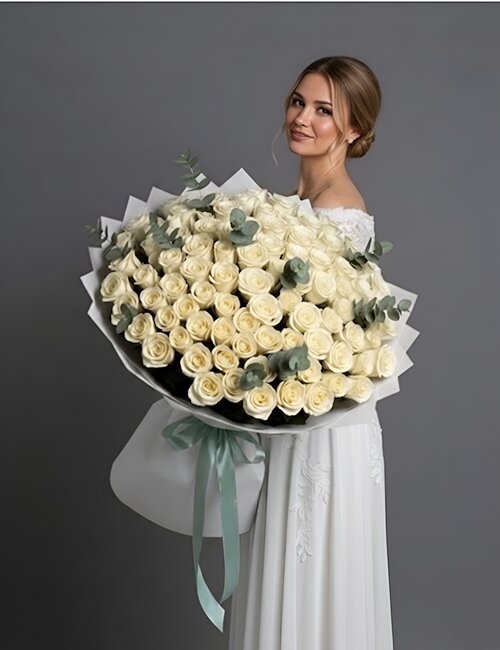 An immense and luxurious white pearl bouquet of 100 white Avalanche roses mixed with fresh green eucalyptus leaves, elegantly wrapped in white floral paper.